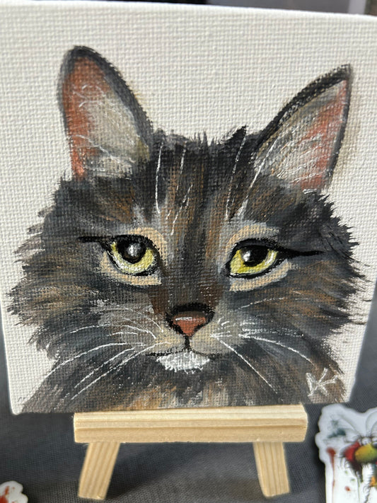 Canvas painting of a cat's face on an easel with other artworks in the background.